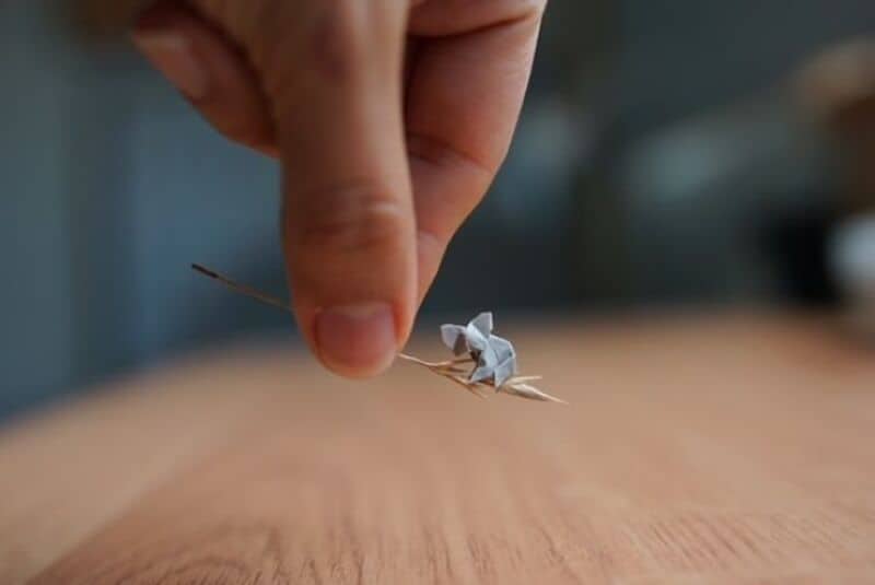 Close-up of a hand holding a tiny paper origami crane over a wooden surface.