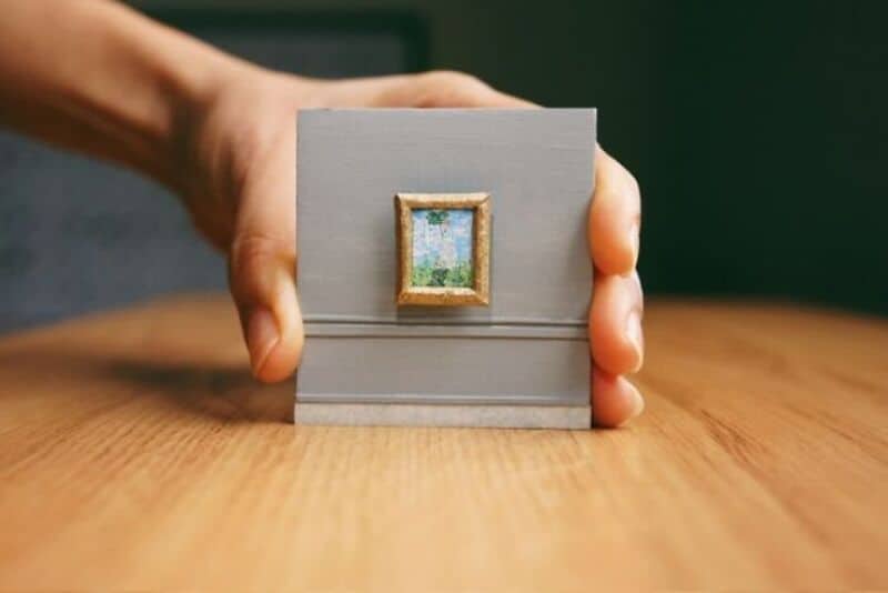 Miniature paper art of a landscape in a small frame held by a hand.