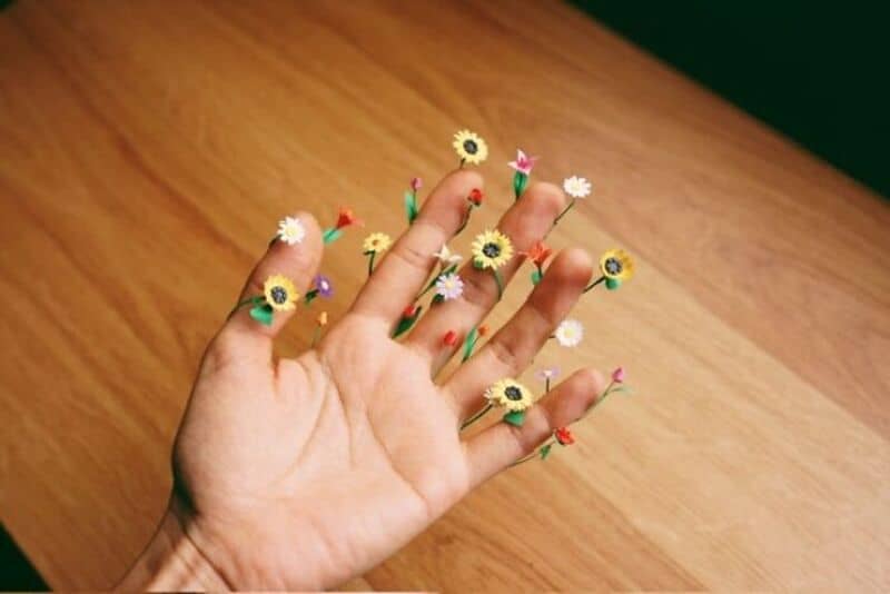 Hand with miniature paper flowers on fingers, on wooden surface.
