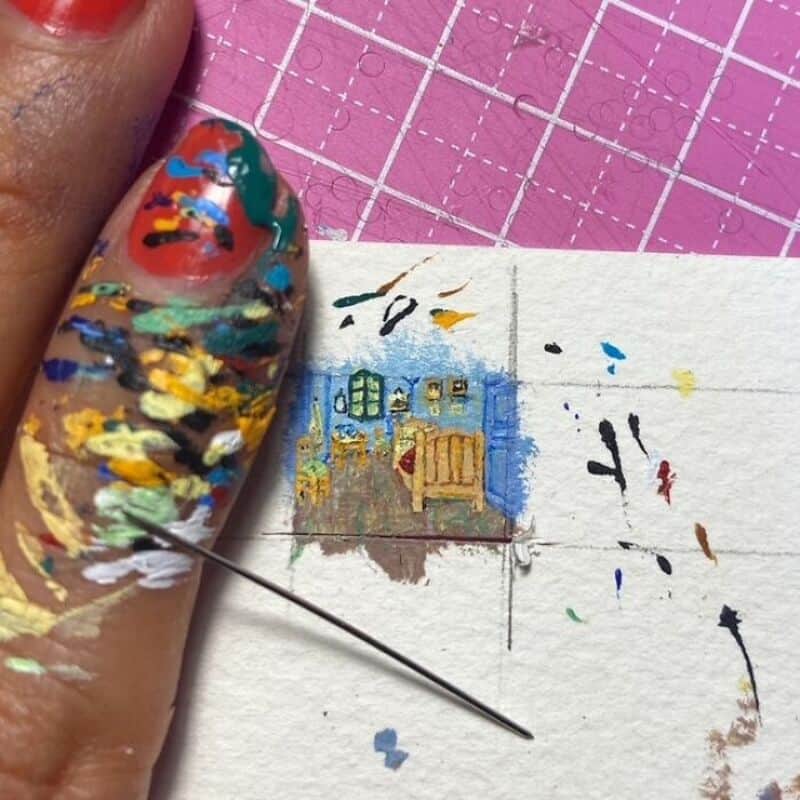 Miniature paper art of a house being painted with a needle and colorful paints.