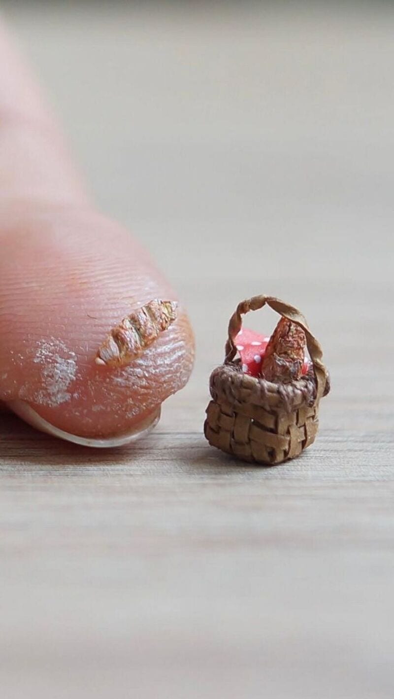 Close-up of a tiny paper basket with a pink flower, next to a finger with a paper nail.