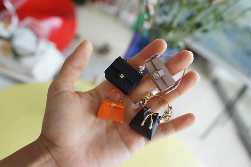 Hand holding miniature handbags and accessories, blurred background.