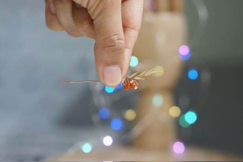 Close-up of a hand holding a tiny paper craft with colorful lights in the background.