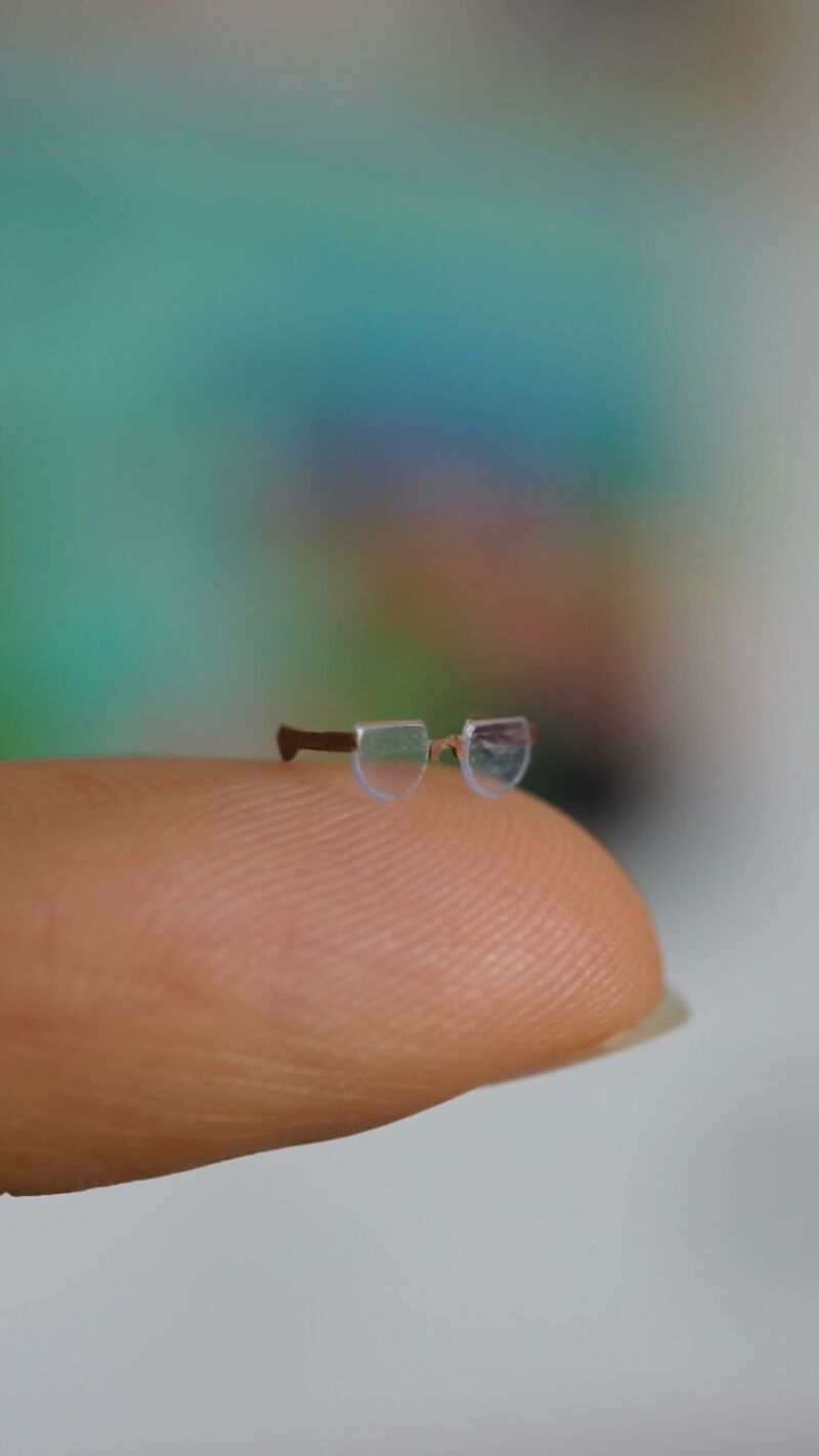 Miniature glasses on a fingertip with a blurred colorful background.