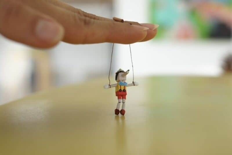 Miniature paper art of a person hanging from a hand, with a blurred background.