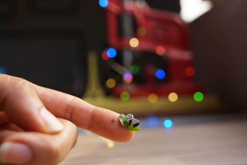 Close-up of a tiny paper art figure on a finger with blurred colorful lights in background.