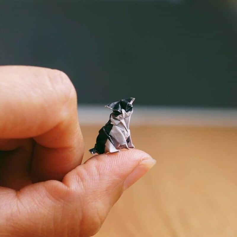 Close-up of a hand holding a tiny paper dog made from black and white paper.