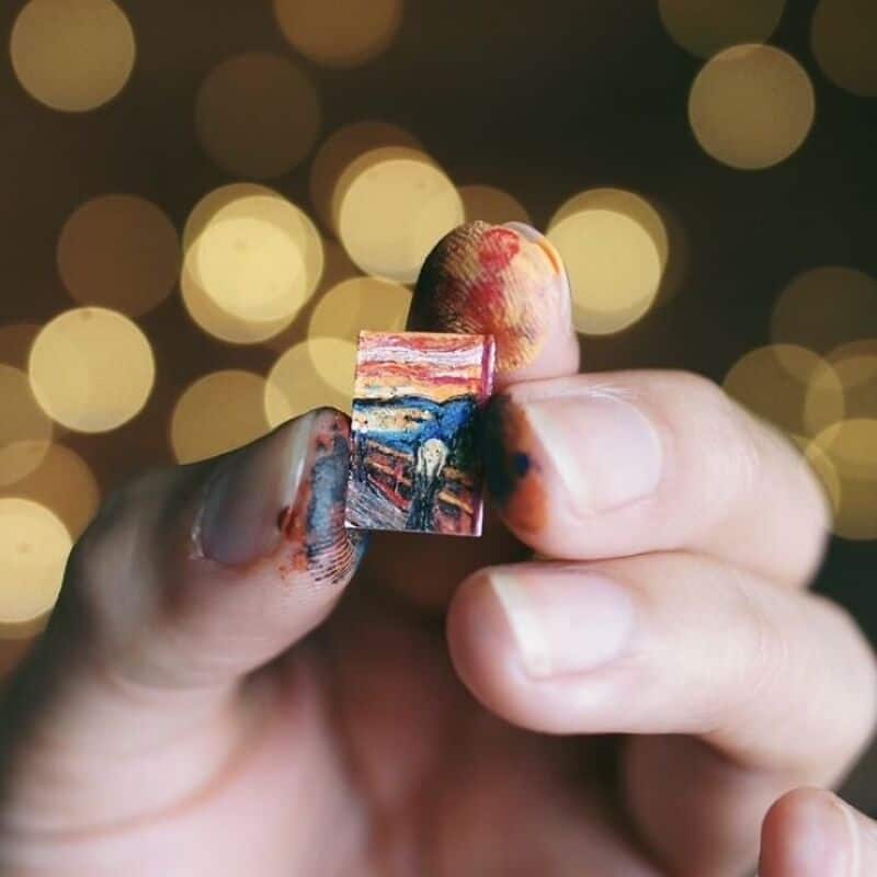 Miniature paper art piece held between fingers with blurred bokeh background.