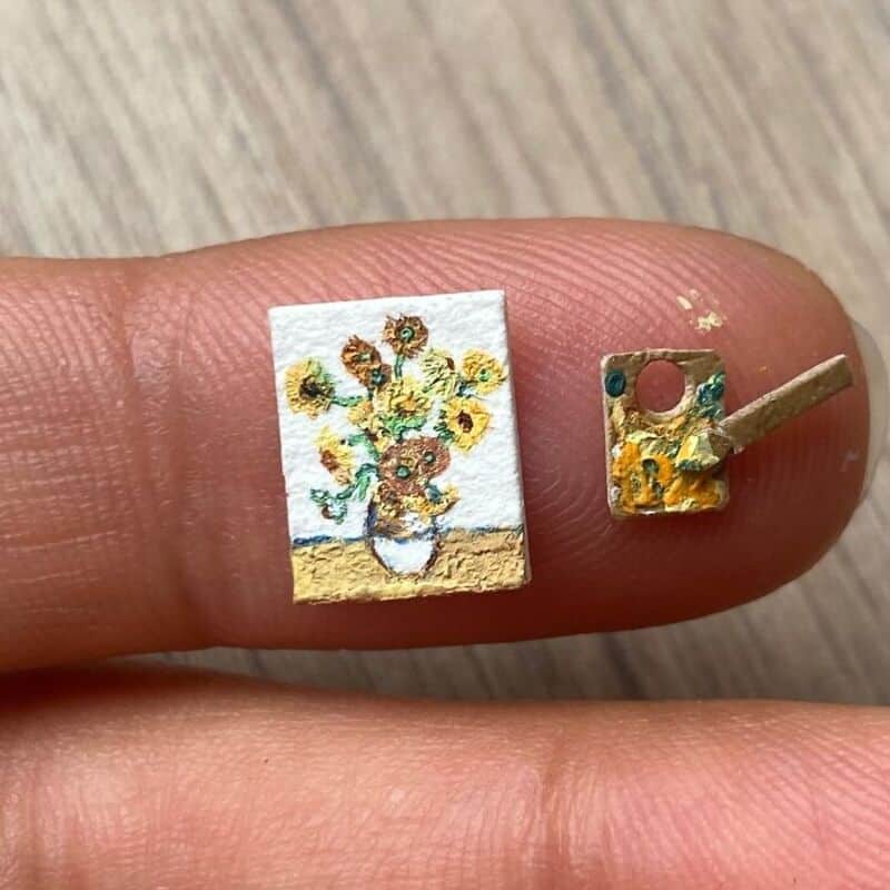 Miniature paper art of a sunflower bouquet in a pot on a finger.