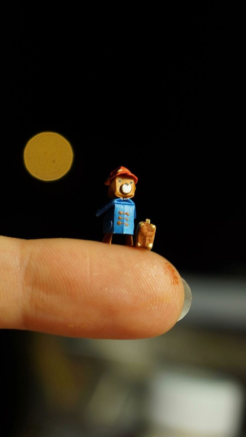 Miniature paper art figure of a girl with a red hat and blue coat on a finger, moon in background.