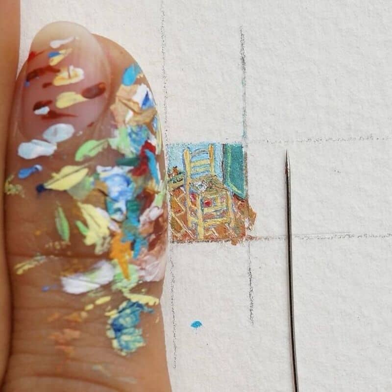 Close-up of a finger with colorful paint and a tiny, detailed paper art scene.