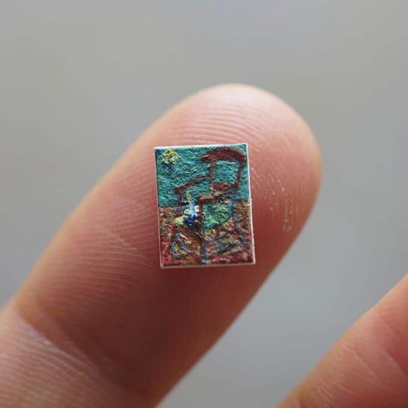 Miniature paper art piece on fingertip, depicting a person with a hat.
