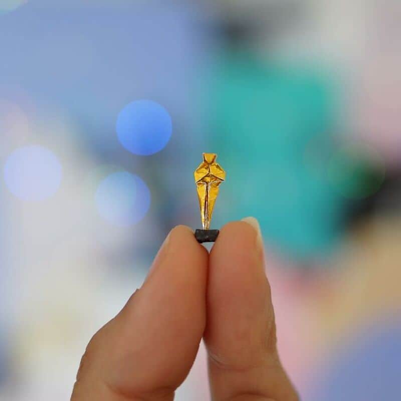 Miniature paper art of a person holding a tiny yellow umbrella.