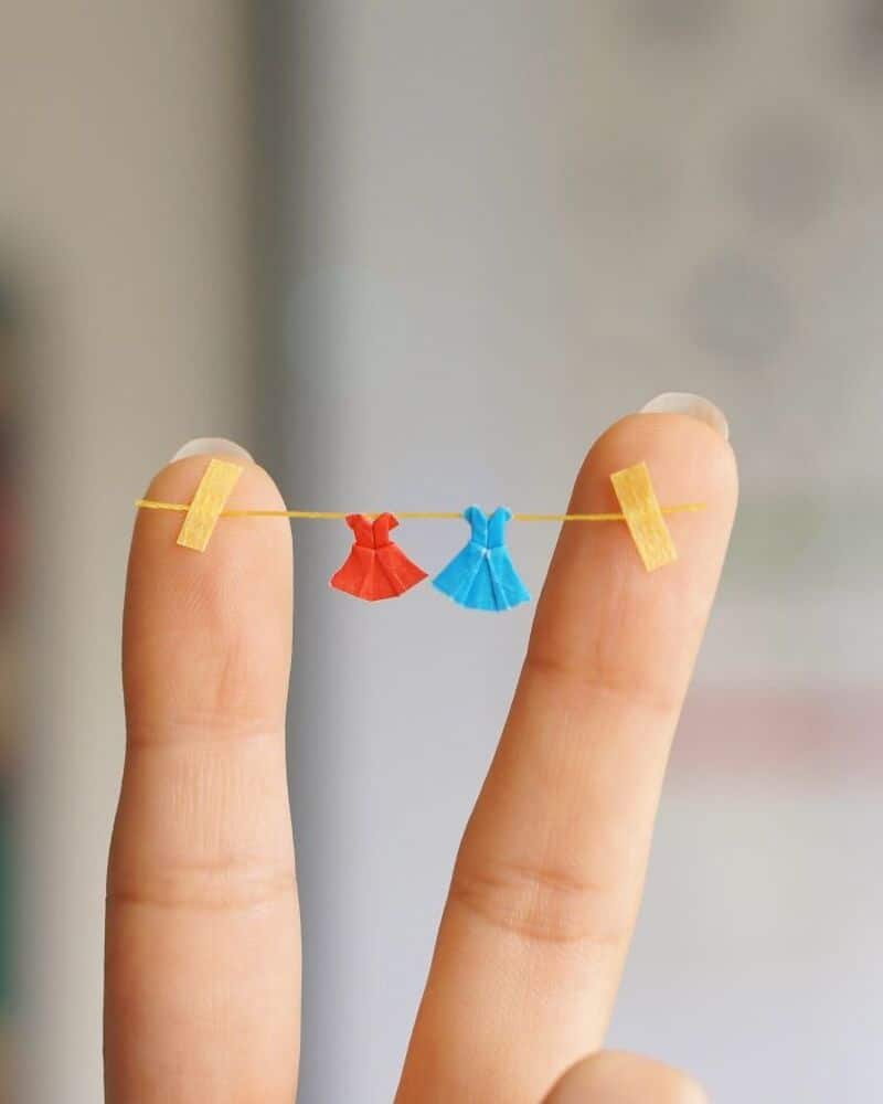 Miniature paper dresses hanging on a string between two fingers.