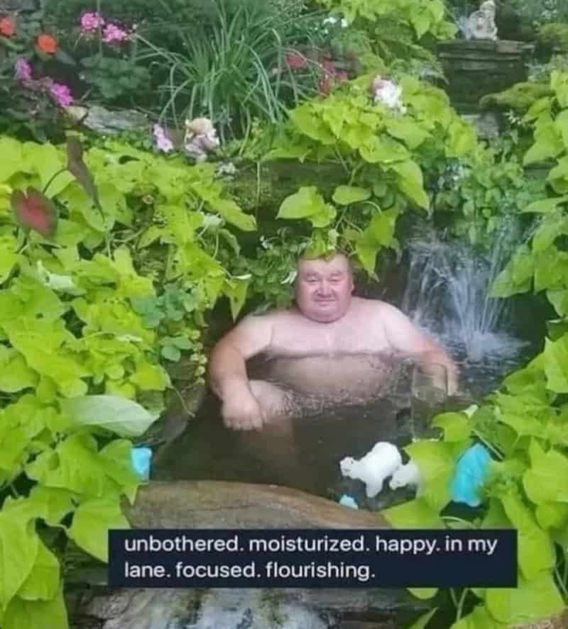 Man relaxing in a lush garden pond with greenery and flowers.