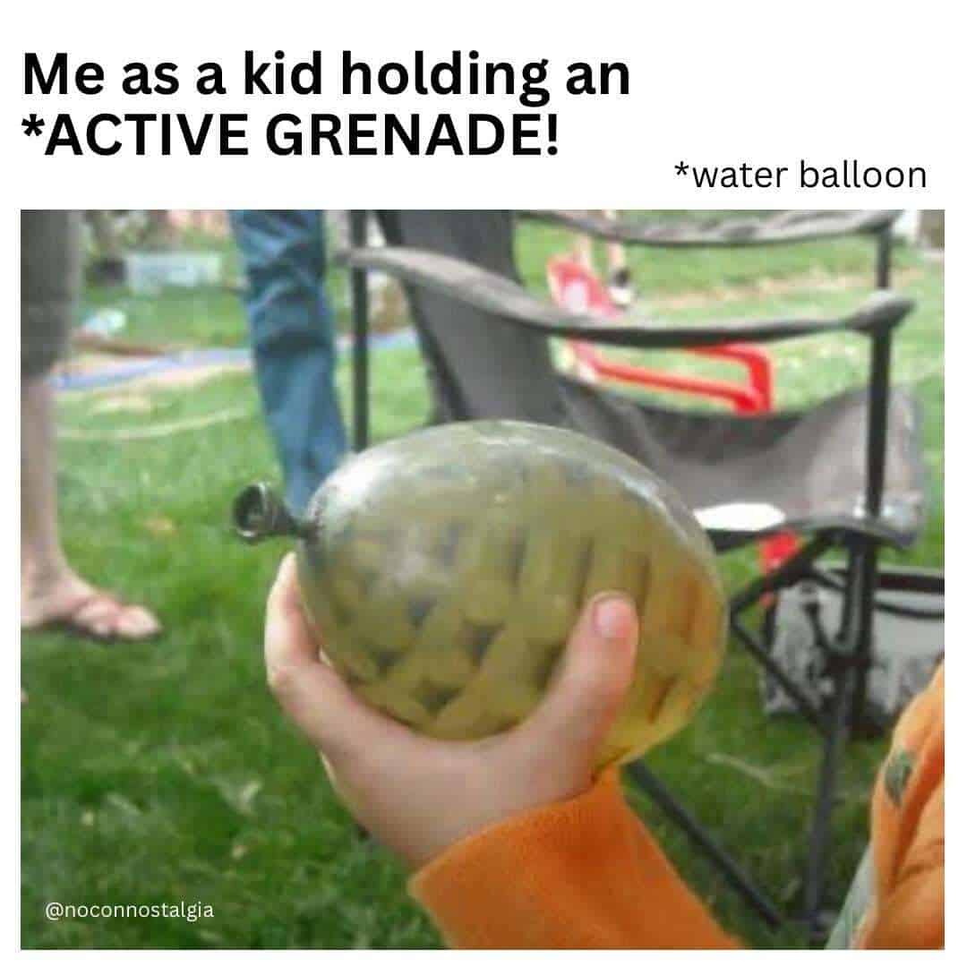 Child holding an active water balloon with a water balloon label, outdoors in a park.