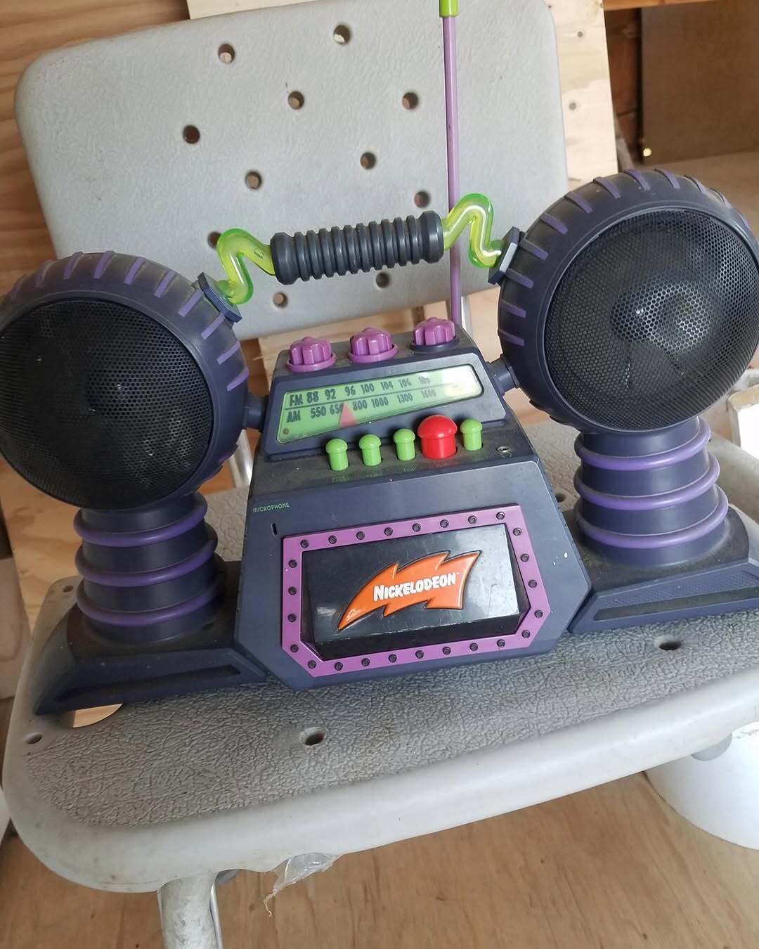 Nickelodeon toy radio with speakers, buttons, and a handle, on a chair.