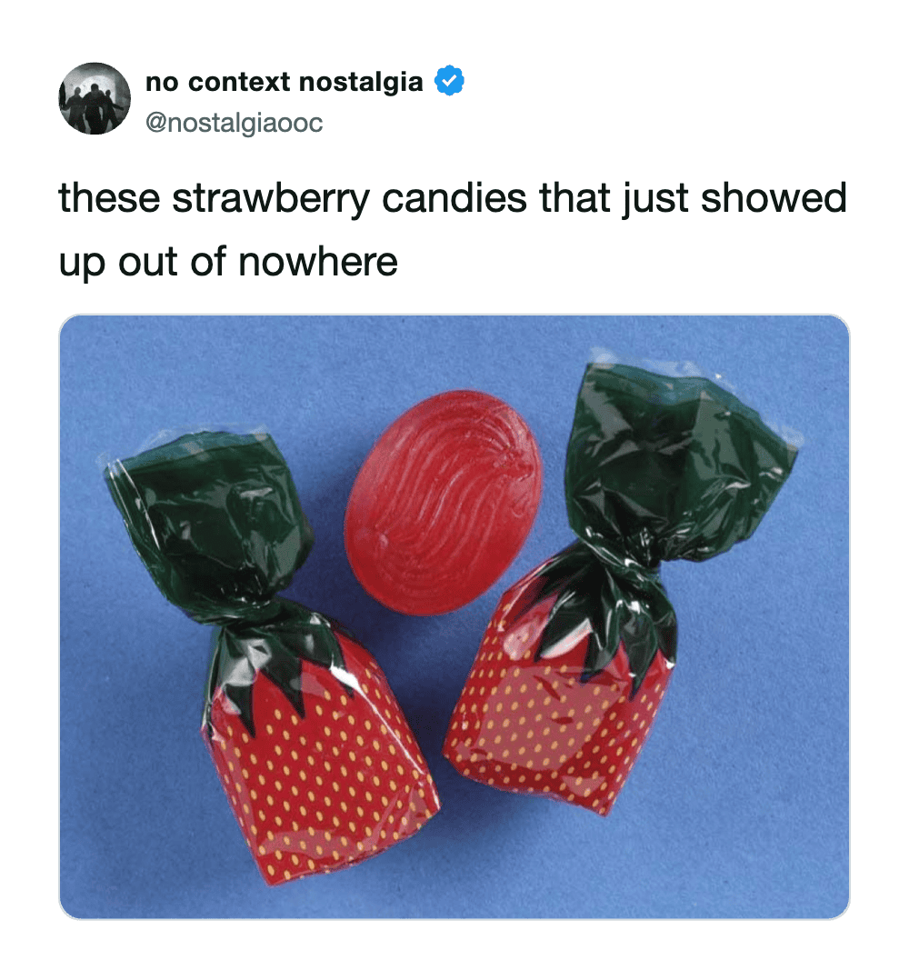 Strawberry candies wrapped in green and red packaging with one unwrapped red candy on a blue backgro.