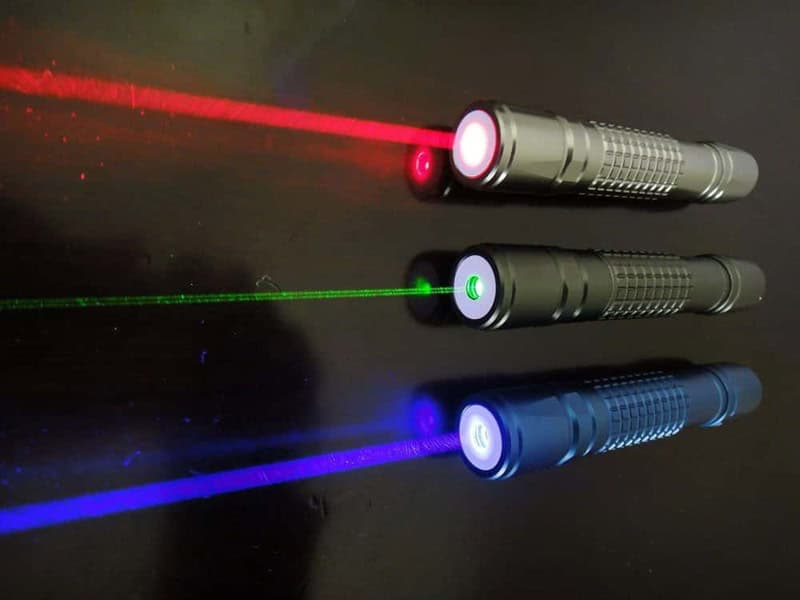 Three laser pointers emitting red, green, and blue beams on a black surface.
