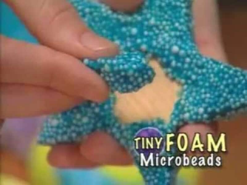 Close-up of a hand squeezing a blue foam microbead toy with text Tiny Foam Microbeads.