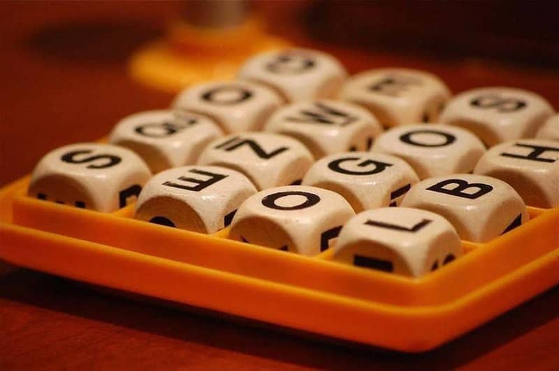 Scrabble letter dice in a yellow tray on a wooden surface.
