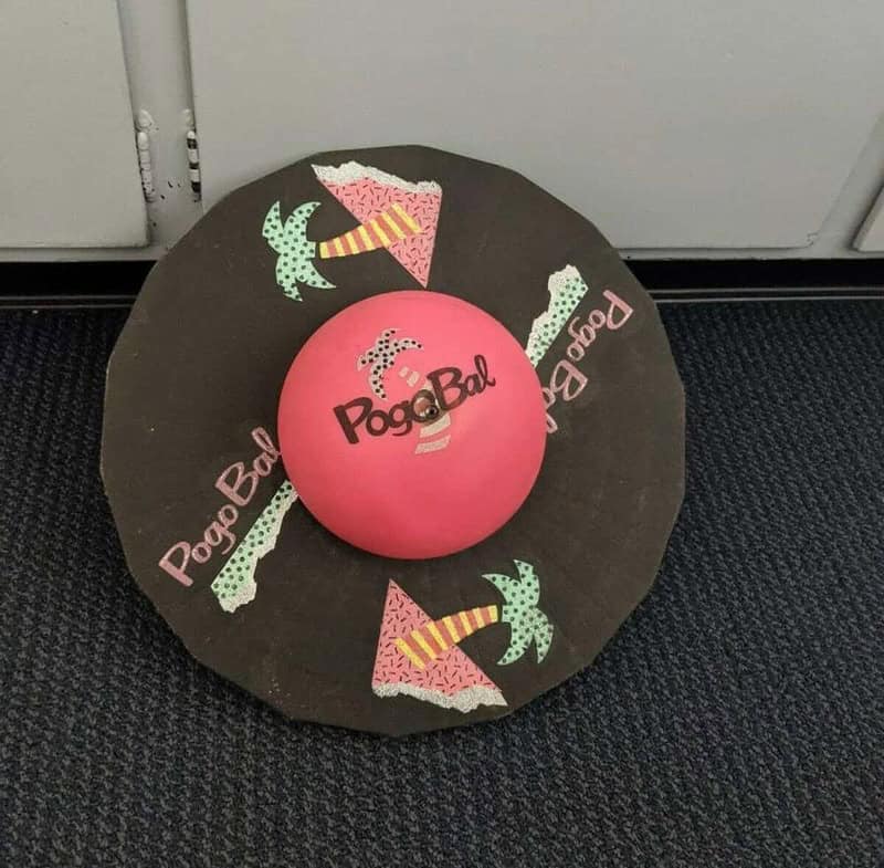 Pink Pogo Ball with black text on a black circular mat with colorful ice cream cone and palm tree.