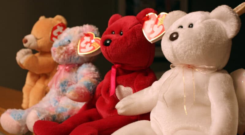 Four Beanie Babies teddy bears in a row, including a tan, multicolored, red, and white bear.
