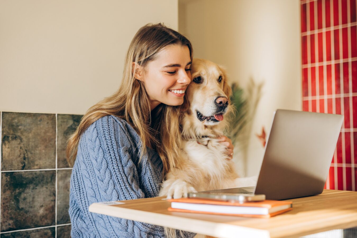 A woman smiling with her dog while looking at a laptop screen.
