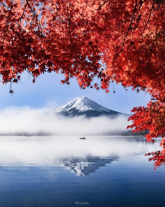 Mount Fuji with red autumn leaves and a boat on the lake.