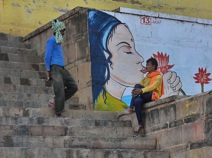 Woman sitting on stairs with mural of a woman holding a lotus flower in the background.