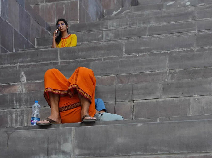Woman in yellow top and orange skirt sitting on stone steps, talking on phone.