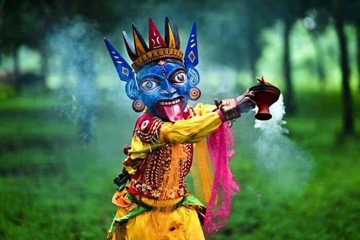 Traditional colorful masked dancer performing in a green outdoor setting.