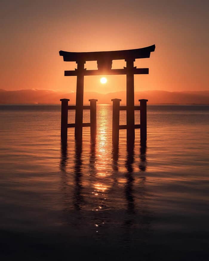 Traditional Japanese torii gate at sunset over water.