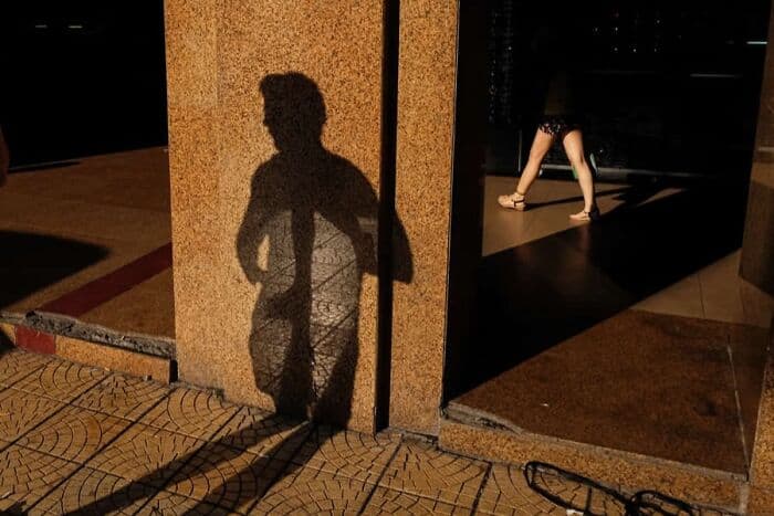 Shadow of a person on a wall with a woman walking in the background.