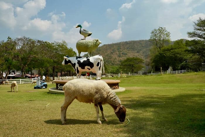 Unique animal sculpture with a cow, sheep, and duck on top in a park setting.