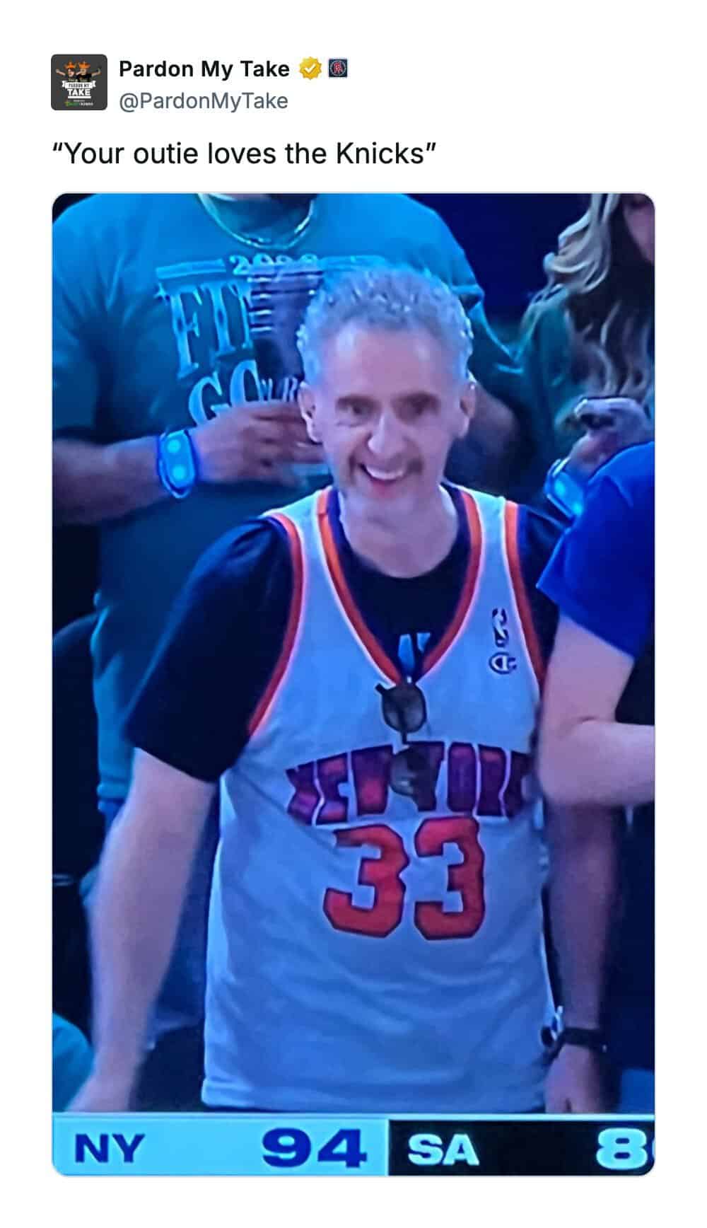 Man in Knicks jersey smiling at a game, score NY 94, SA 8.