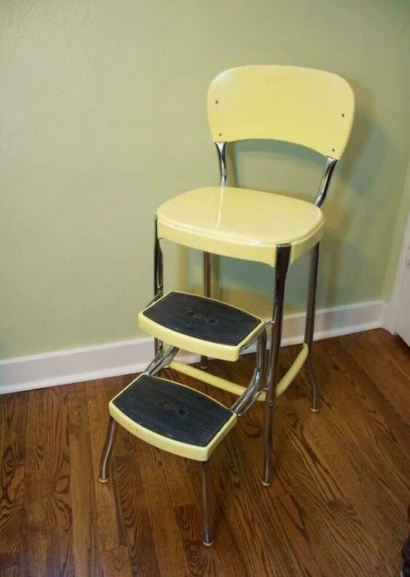 Yellow high chair with black footrests against a green wall.