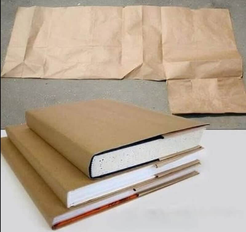 Stack of three books with brown paper wrapping and a long brown paper bag behind them.