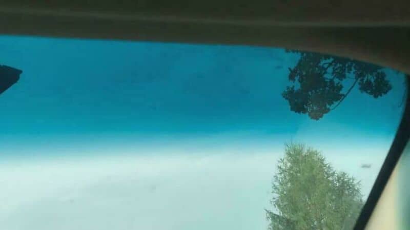 View of the sky and trees through a car windshield.