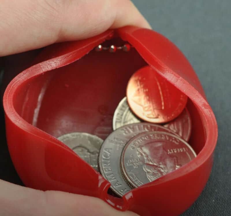 Red coin purse with coins spilling out, on a gray background.