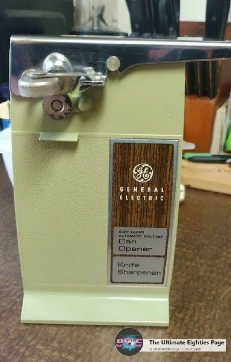 A vintage General Electric can opener with a knife sharpener on a wooden surface.