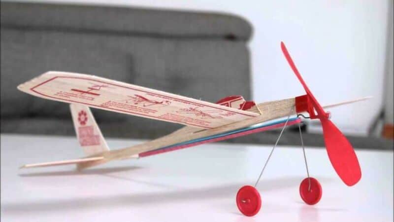 A paper helicopter with red wheels and a red propeller on a white surface.