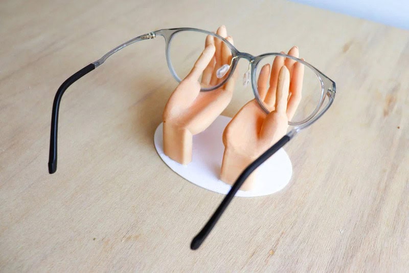 Glasses on a hand sculpture with a funny face, on a wooden surface.
