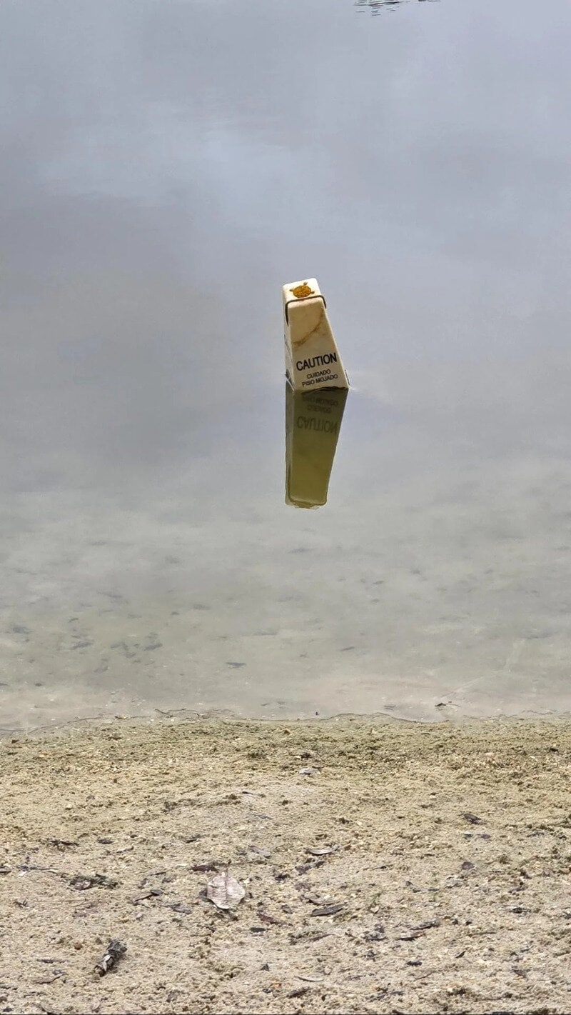 A caution sign floating on a reflective water surface with a cloudy sky.