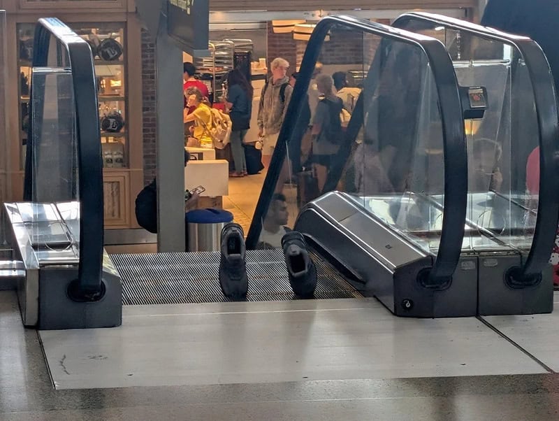 Empty conveyor belt at airport security with glass shields and people in background.
