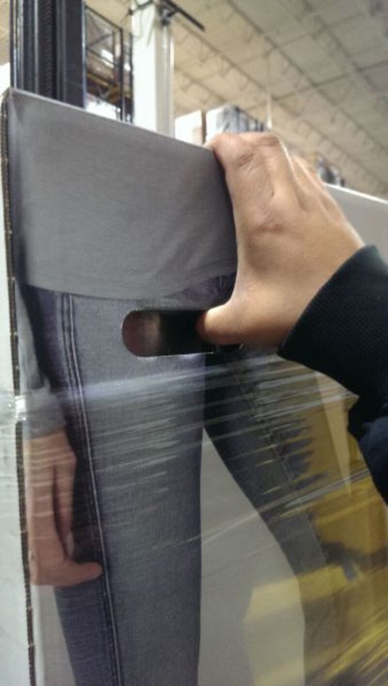 Person holding a gray box with a cutout handle on a store shelf.