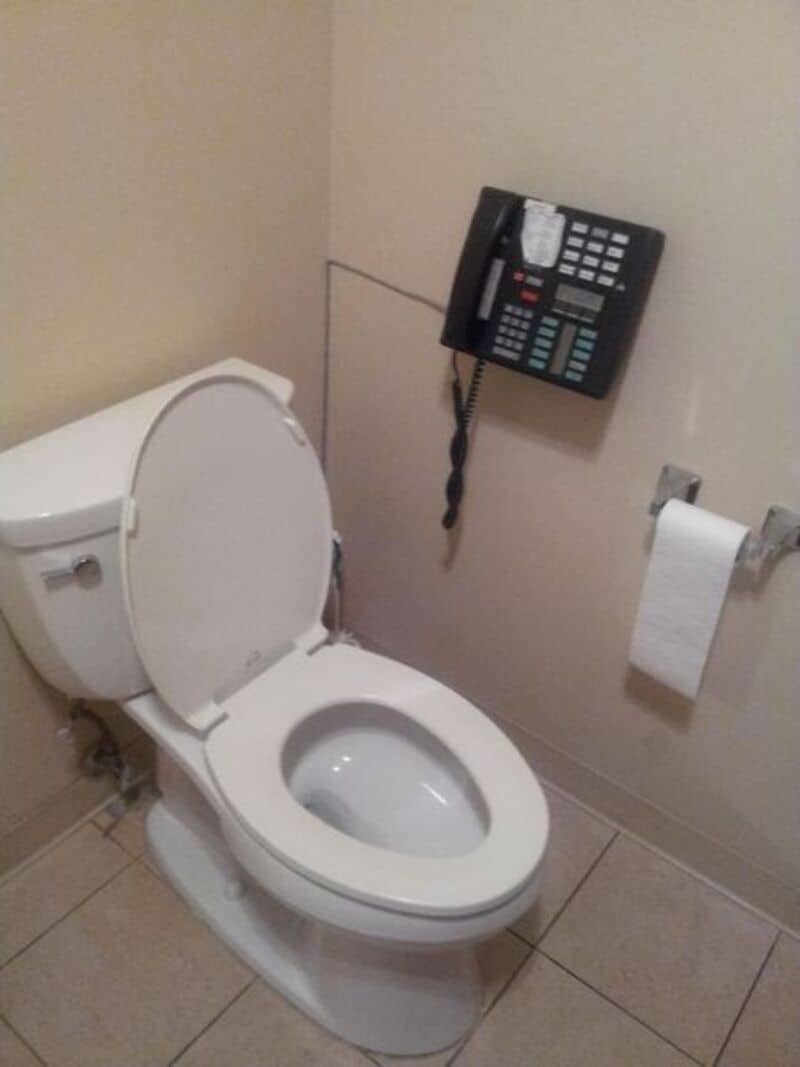 Toilet with a phone attached to the wall above it in a bathroom.