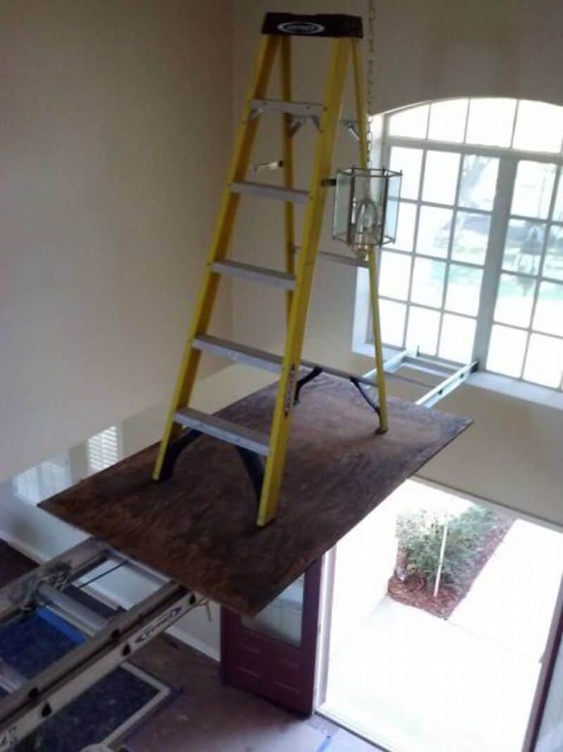 Ladder on a wooden platform in a room with large windows and a door.