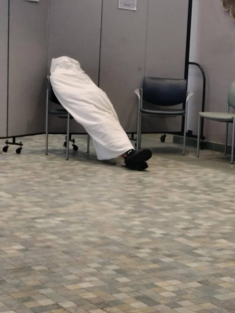 Person with their head and upper body hidden inside a white bag, sitting on a chair.