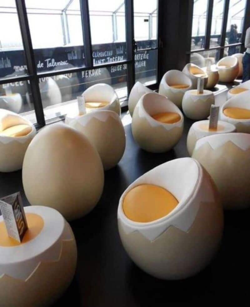 Egg-shaped chairs with yellow cushions inside, arranged in a room with large windows.